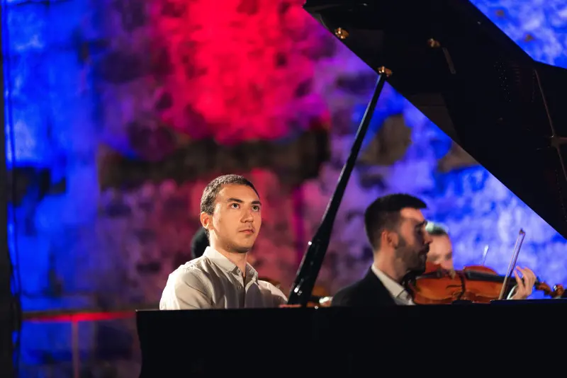 Francisco at the piano beside a violinist, lit in red and blue