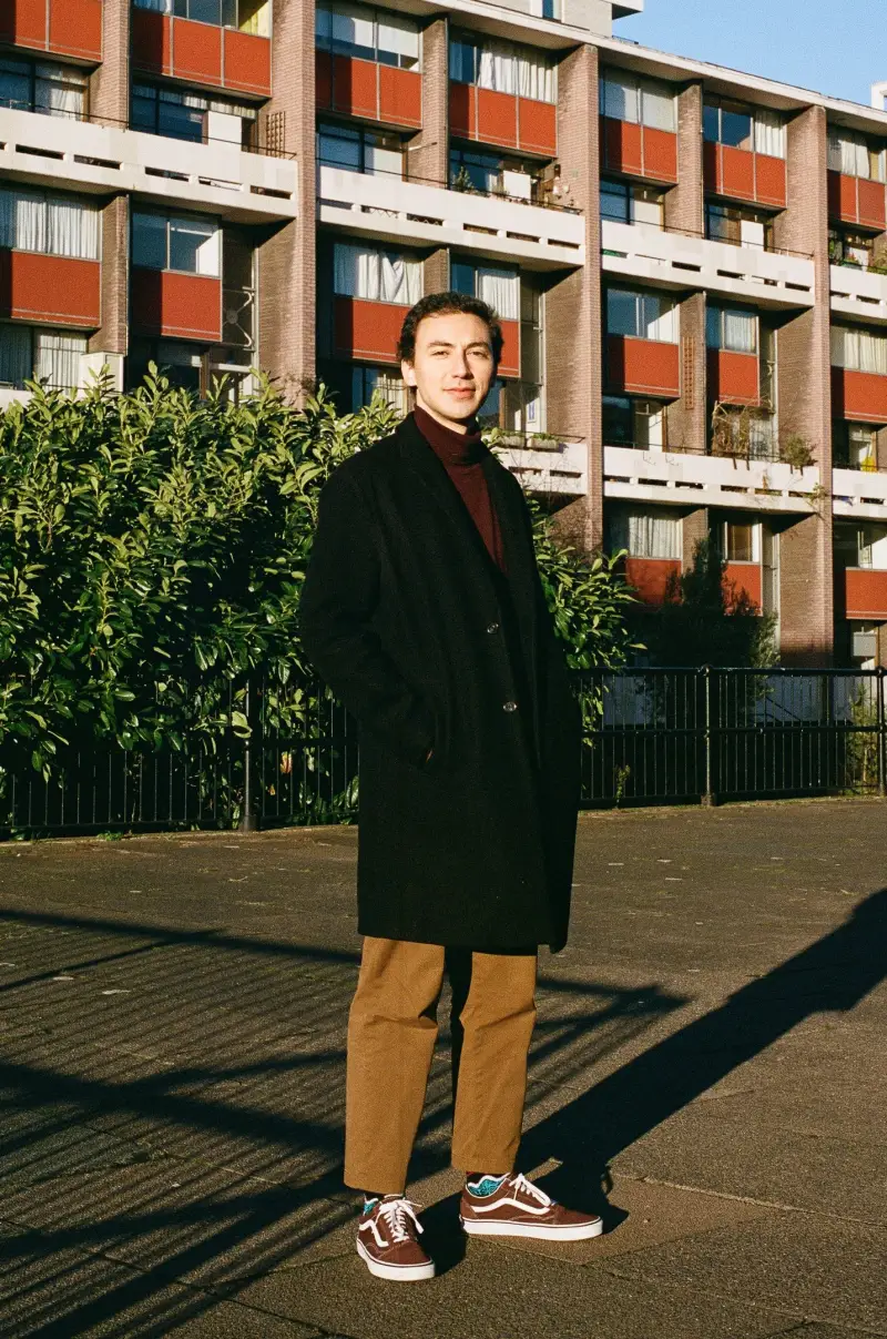Francisco in a long coat in the sunlight outside a brick building