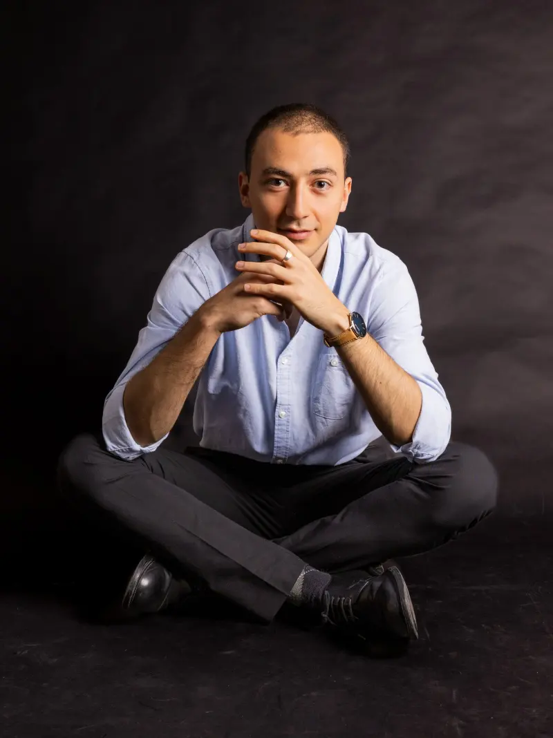 Studio portrait of Francisco sitting cross-legged, hands clasped