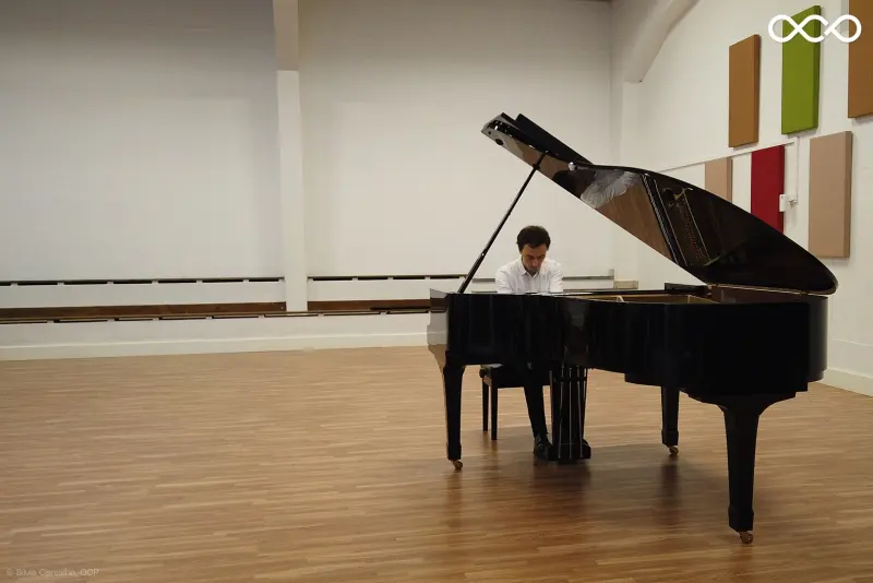 Wide view of Francisco at the piano in a bright recital hall
